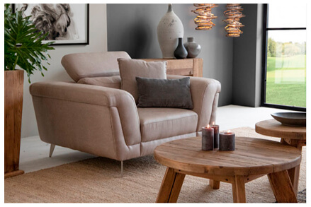 Side view of rustic living room interior showing sandstone one seater couch and two round coffee tables with decorative accessories on top of it